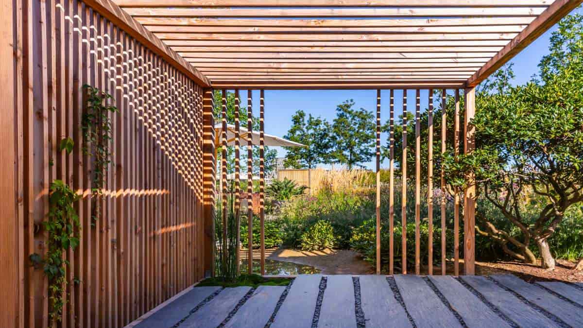 Op een mooie dag, terwijl de zon schijnt, staat er een moderne houten overkapping in de tuin.