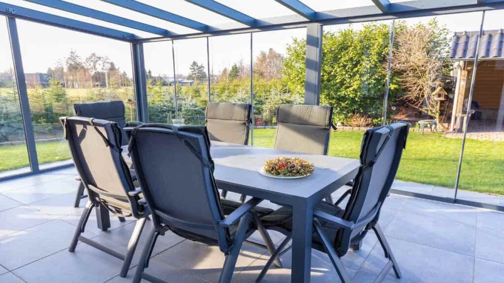 Een donkergrijze eettafel met grote stoelen in een veranda in een zonnige tuin.