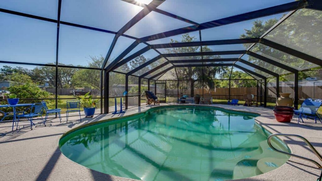 Een poolhouse met een zwembad omringt met grote ramen waar de zon door heen schijnt.